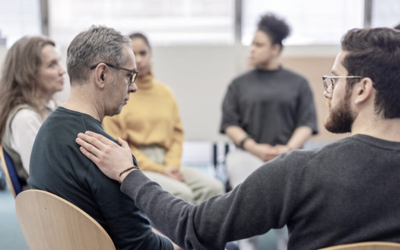 man comforting another man in group therapy